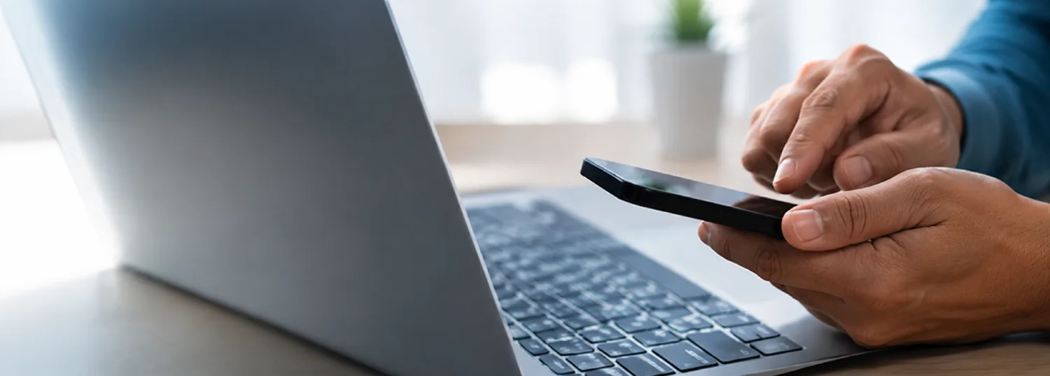 Person using a phone next to a laptop